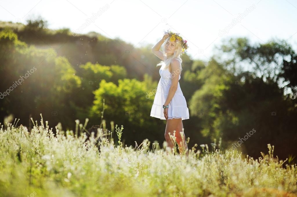 girl in a white sundress and a wreath of flowers on her head aga
