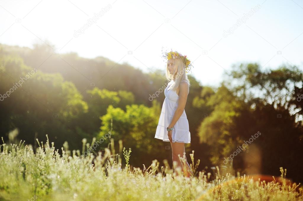 girl in a white sundress and a wreath of flowers on her head aga