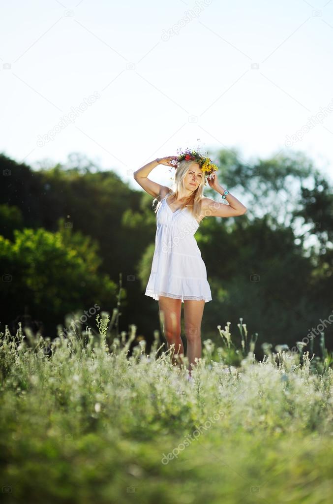 girl in a white sundress and a wreath of flowers on her head aga