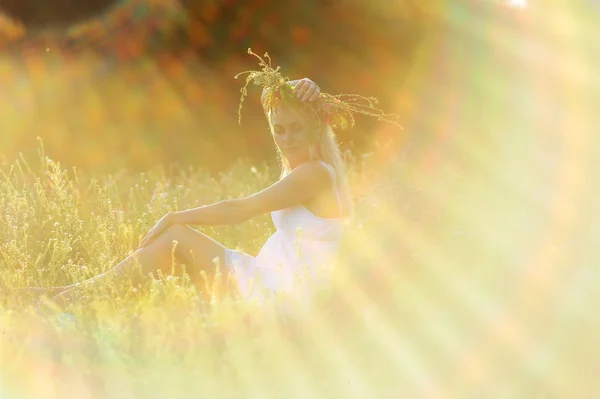 Chica en un vestido blanco y una corona de flores en su cabeza sentarse — Foto de Stock