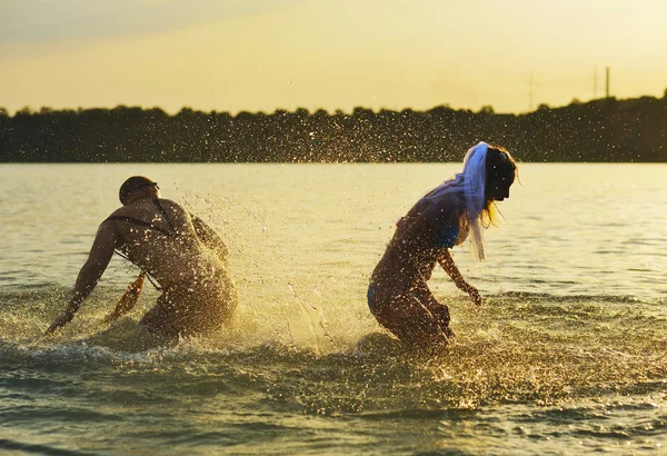 Junge und Mädchen übergießen sich bei Sonnenuntergang mit Wasser — Stockfoto