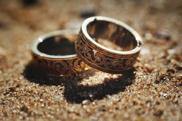 Esküvő gyűrű, gyönyörű faragványok a homok háttér — Stock Fotó
