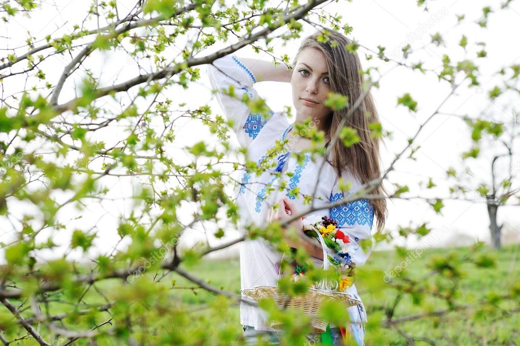 Slavic girl in Ukrainian shirt hiding behind a tree