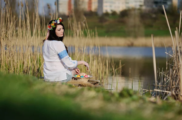 Slawisches Mädchen im ukrainischen Hemd sitzt mit Ostern auf der Brücke — Stockfoto