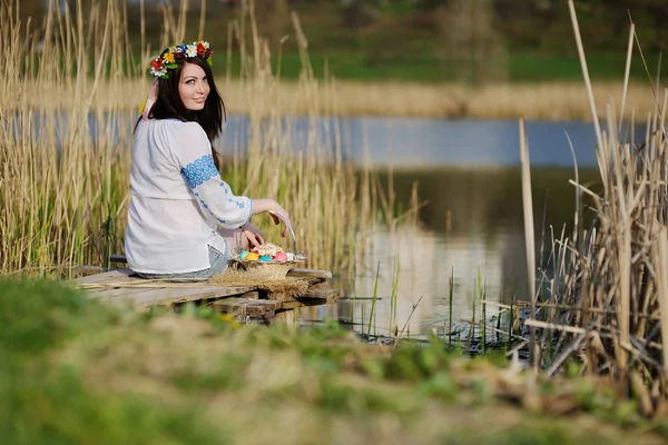 Chica eslava en camisa ucraniana sentada en el puente con Pascua — Foto de Stock