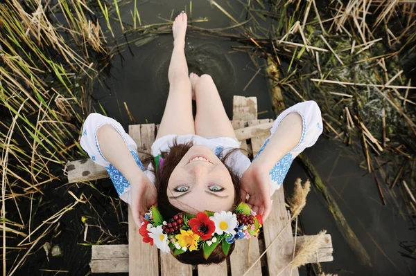 Девушка в цветочном венке на голове сидит на мосту и мы — стоковое фото