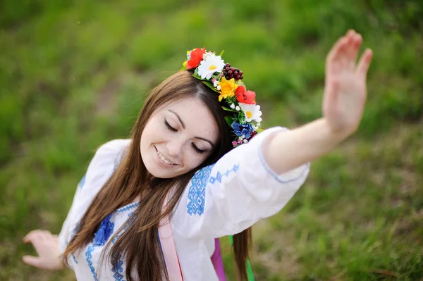 Oekraïense meisje in een shirt en een bloemen krans op haar hoofd pullin — Stockfoto