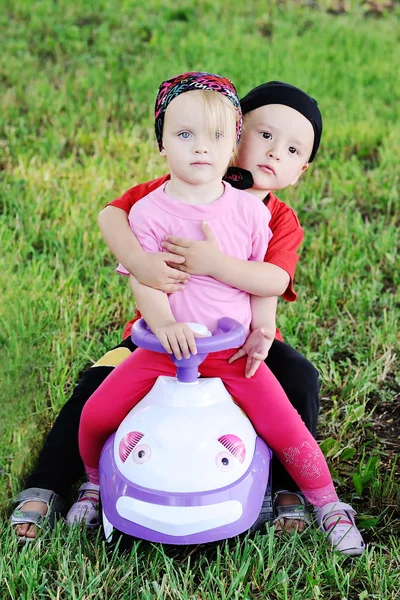Anak kecil dan gadis mengendarai mobil mainan. Bayi laki-laki memeluk gadis — Stok Foto