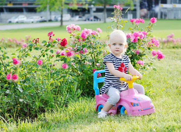 Menina dirigindo carro de brinquedo rosa em um fundo de rosas — Fotografia de Stock