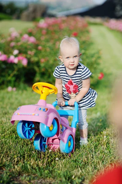 Bayi perempuan dengan mobil mainan di latar belakang mawar — Stok Foto