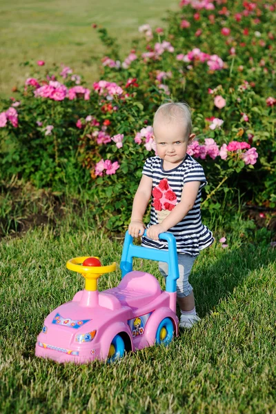 Mädchen mit einem Spielzeugauto auf einem Hintergrund aus Rosen — Stockfoto