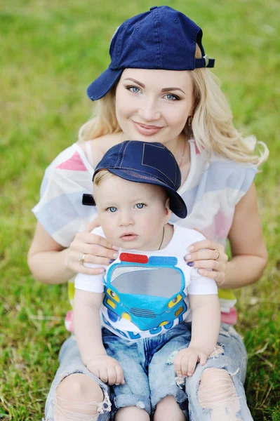 Мама и маленький сын в кепке на фоне зеленой травы — стоковое фото