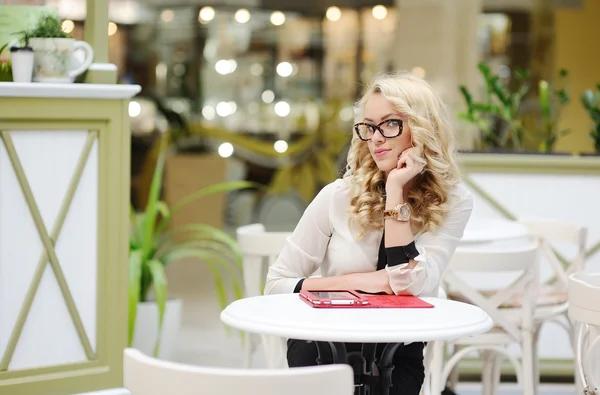 Hermosa chica en gafas se sienta en una mesa con una tableta — Foto de Stock