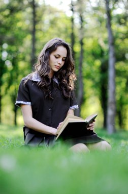 Kız öğrenci çimlere oturup kitap okumak. Güzel kız bir kitap okuma