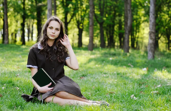 Colegiala leyendo un libro sentado en la hierba. Hermosa chica leyendo un libro — Foto de Stock