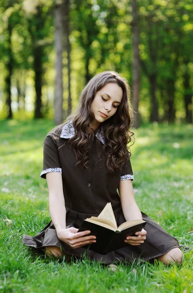 女生读一本书，坐在草地上。读一本书的美丽女孩 — 图库照片