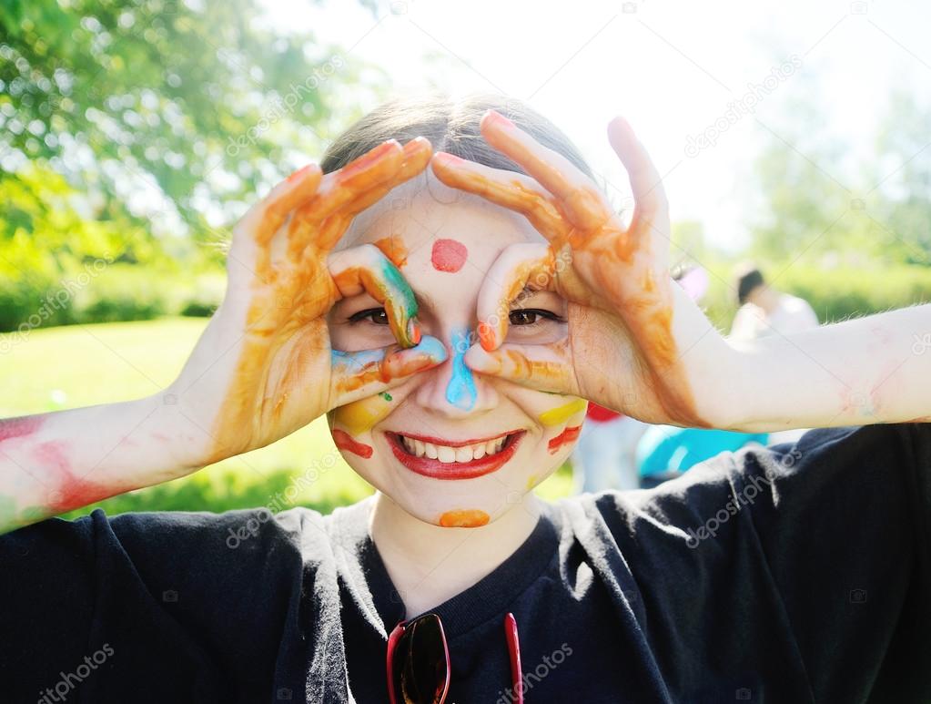 Cheerful young girl with bright colors smeared face.