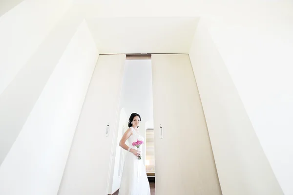 Mooie bruid met een bruiloft boeket staat in de deuropening — Stockfoto