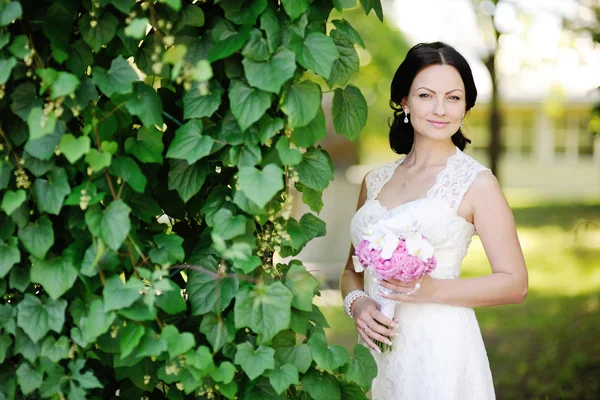 Bela noiva com um buquê de casamento em um fundo de verde — Fotografia de Stock