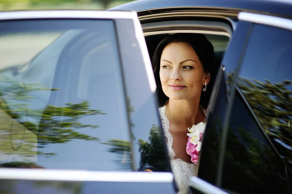 Mooie bruid met een boeket van de bruiloft in een donkere auto — Stockfoto