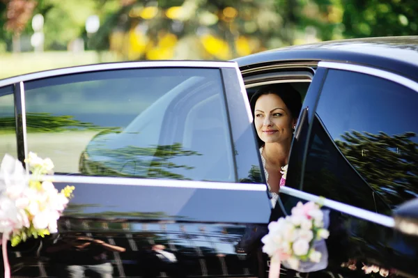 Mooie bruid met een boeket van de bruiloft in een donkere auto — Stockfoto