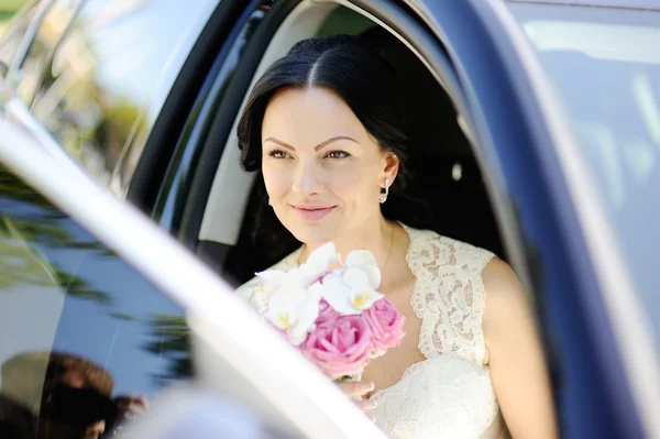 Schöne Braut mit einem Brautstrauß im dunklen Auto — Stockfoto