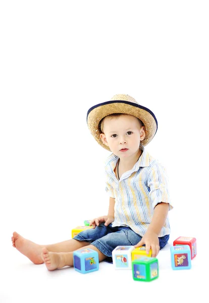 Baby boy in a straw hat playing with multicolored cubes on a whi — Stock Photo, Image