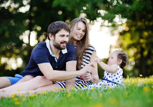 Genç aile - anne, baba ve kızı çimlere oturup. Delikanlı — Stok fotoğraf