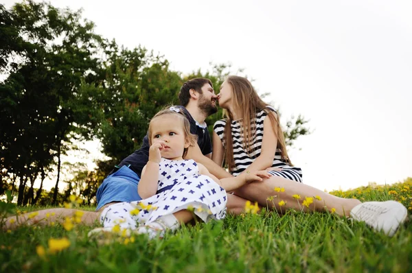 Çimenlerin üzerinde parkta genç aile rahatlatıcı. küçük kız oyun — Stok fotoğraf