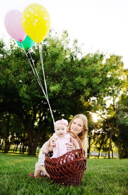 Kızı parkta çim rahatlatıcı annesiyle. Balonlu Sepet içinde küçük kız