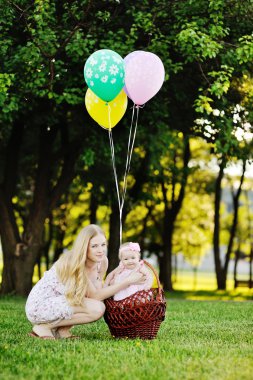 Kızı parkta çim rahatlatıcı annesiyle. Balonlu Sepet içinde küçük kız