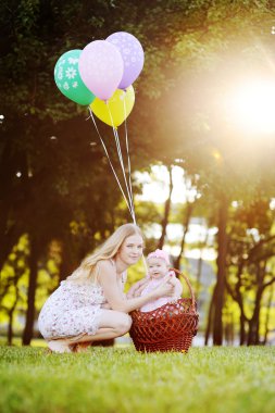 Kızı parkta çim rahatlatıcı annesiyle. Balonlu Sepet içinde küçük kız