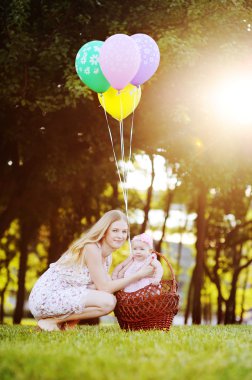 Kızı parkta çim rahatlatıcı annesiyle. Balonlu Sepet içinde küçük kız
