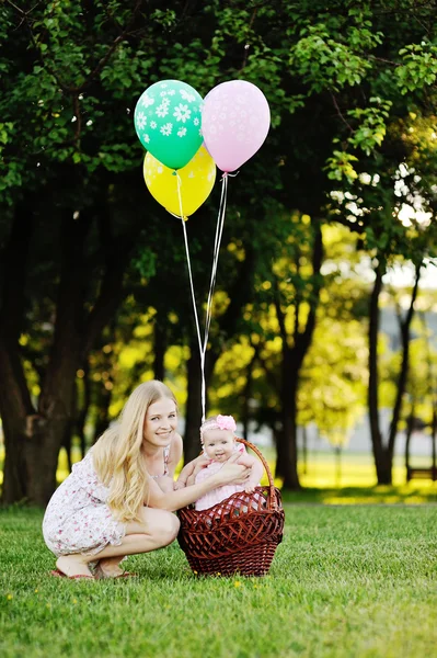 Дочь с матерью отдыхает в парке на траве. маленькая девочка в корзине с воздушными шарами — стоковое фото