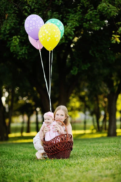 Filha com sua mãe relaxando no parque na grama. menina na cesta com balões — Fotografia de Stock