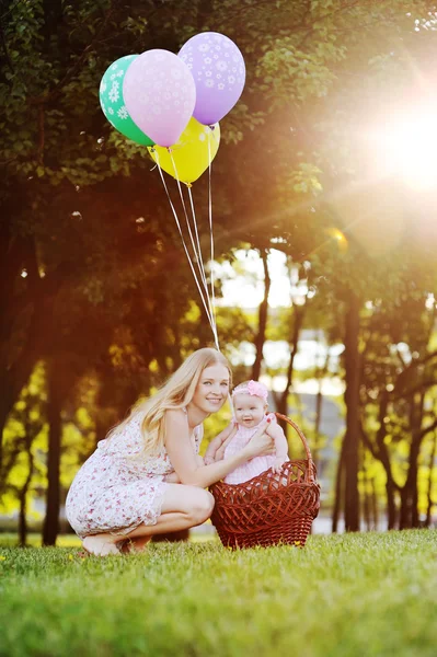 Filha com sua mãe relaxando no parque na grama. menina na cesta com balões — Fotografia de Stock