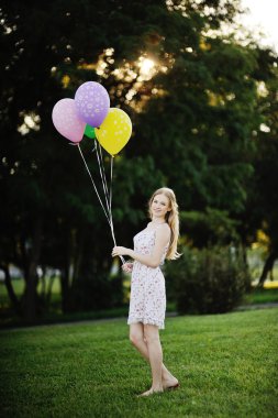 genç kızın ağaçları ve gün batımının bir arka plan üzerinde renkli balonlar ile