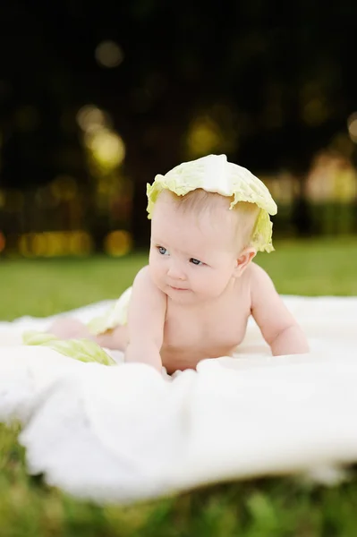 Bayi perempuan dengan kubis. Kubis daun di kepala seorang anak. Anak bersantai di taman di rumput . — Stok Foto