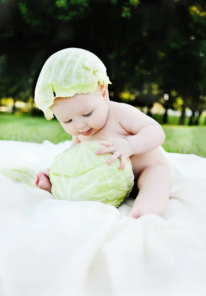 Petite fille au chou. Les feuilles de chou sur la tête d'un enfant. Enfant relaxant dans un parc sur l'herbe . — Photo