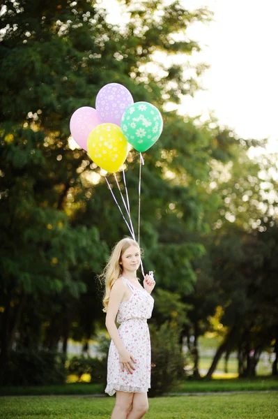 Niña con globos de colores sobre un fondo de árboles y la puesta del sol —  Fotos de Stock