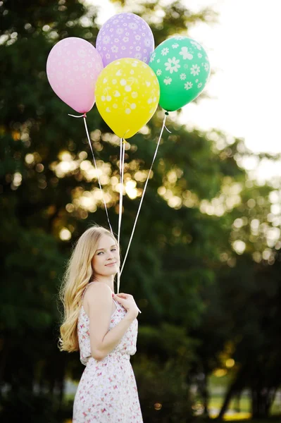 Young girl with colored balloons on a background of trees and the sunset — Stock Photo, Image