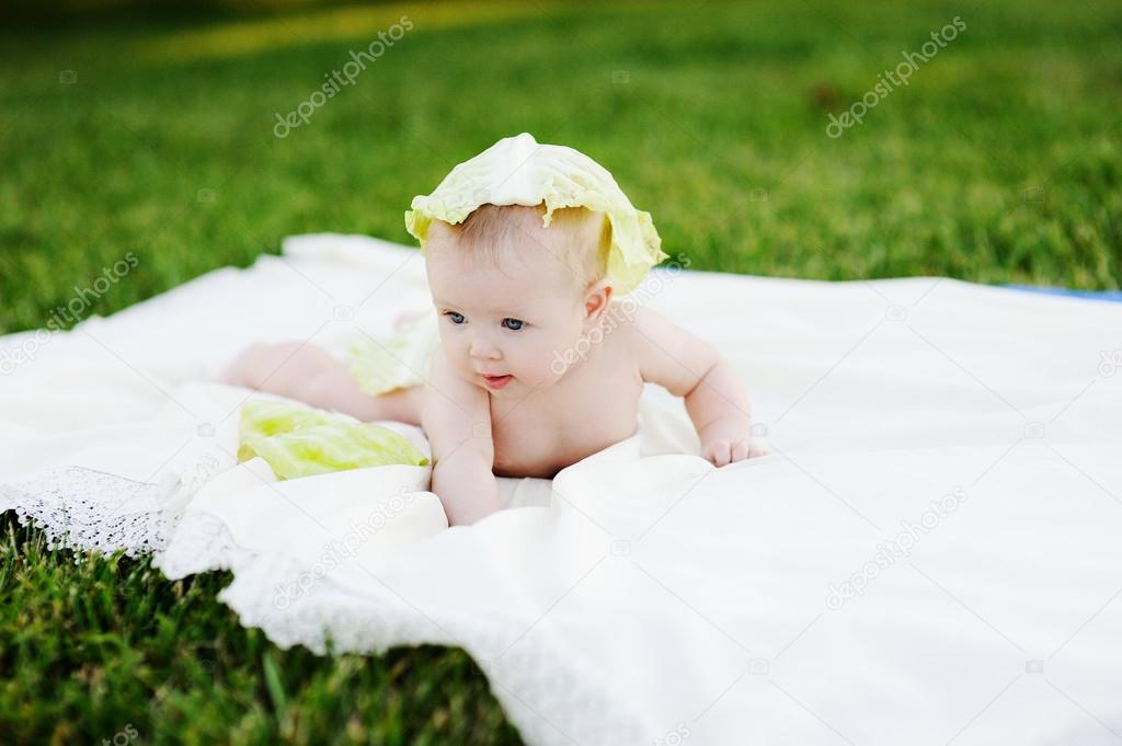 baby girl with cabbage. Cabbage leaves on the head of a child. Child relaxing in a park on the grass.