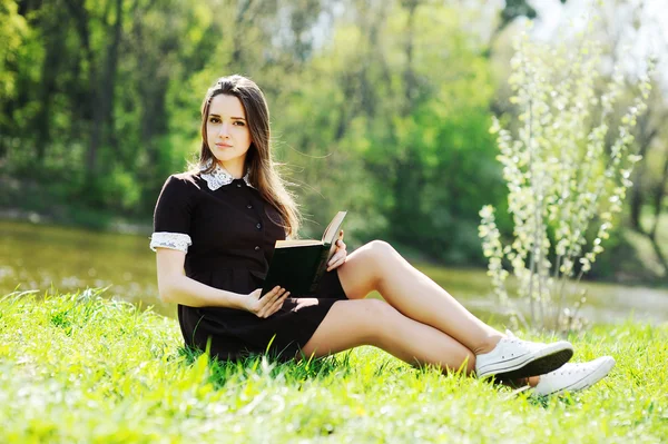 Estudante com um livro relaxante no parque na grama — Fotografia de Stock