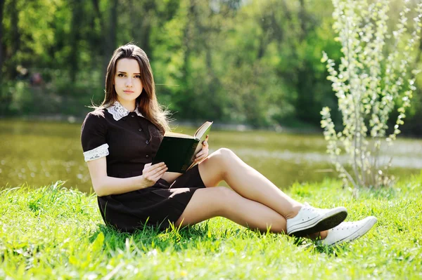 Estudante com um livro relaxante no parque na grama — Fotografia de Stock