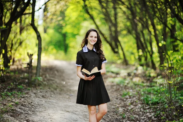 Mooie schoolmeisje met een boek in handen op een achtergrond van groene bomen — Stockfoto