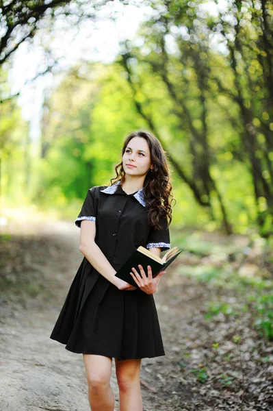 Hermosa colegiala con un libro en las manos sobre un fondo de árboles verdes — Foto de Stock