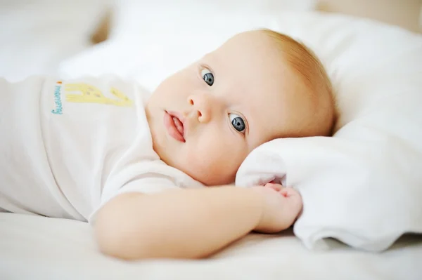 Portrait of baby with blue eyes. A child resting on a bed — Stock Photo, Image