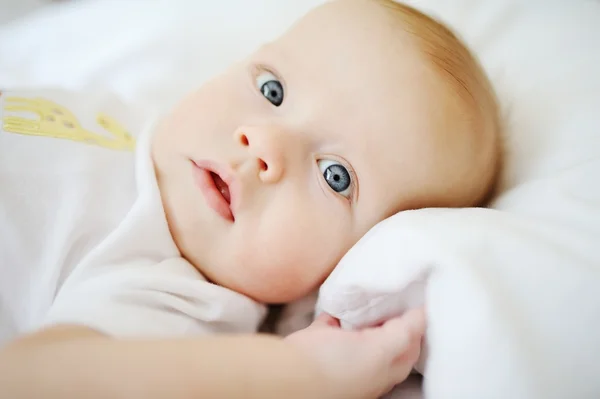 Portrait of baby with blue eyes. A child resting on a bed — Stock Photo, Image