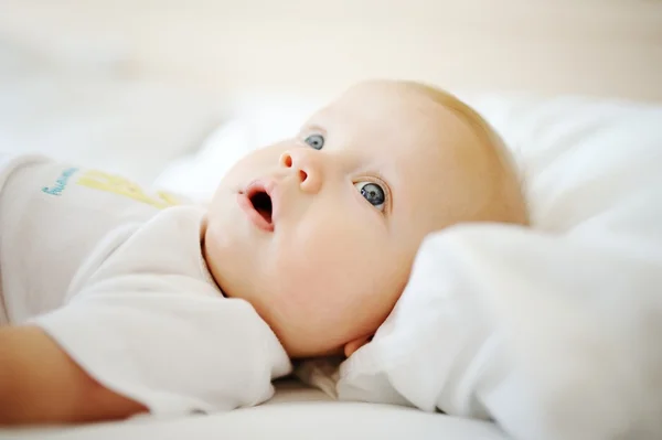 Portrait of baby with blue eyes. A child resting on a bed — Stock Photo, Image