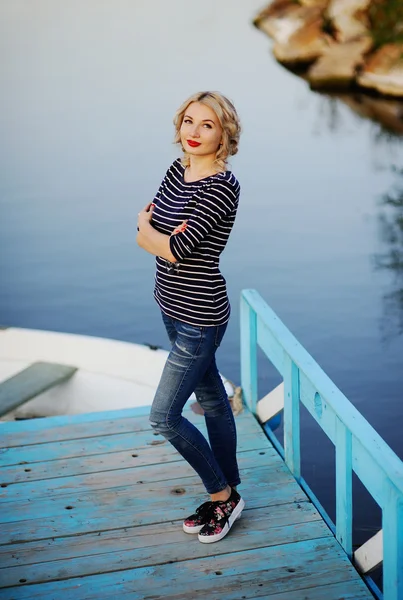 Chica en una blusa a rayas de pie sobre un puente de madera en un backgr —  Fotos de Stock
